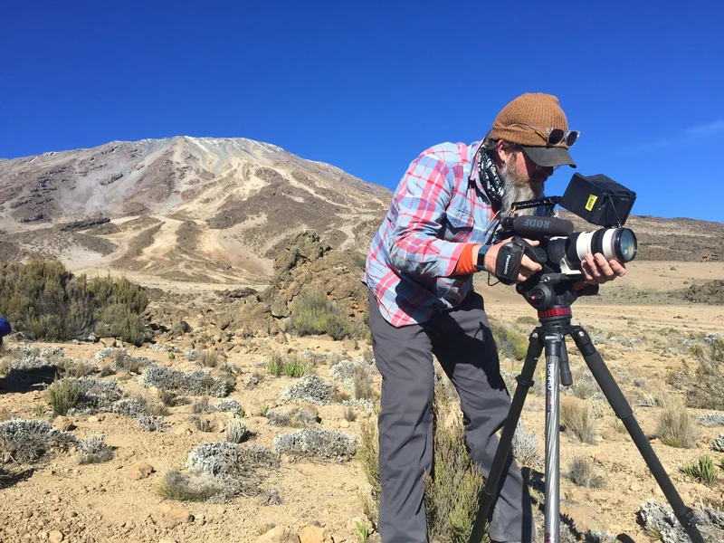 Mike Murphy filming with a cinema camera on a tripod on the slopes of Mount Kilimanjaro